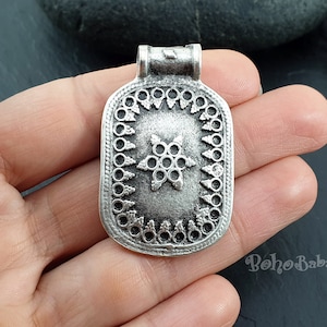 May include: Silver pendant with a star design and a decorative border. The pendant has a loop at the top for attaching a chain.