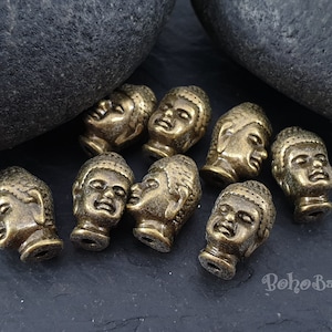 May include: A collection of eight antique gold-toned Buddha head beads. The beads are detailed with intricate carvings and have a distressed finish.