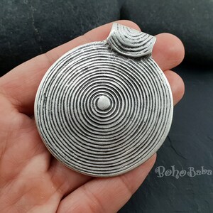 May include: Silver pendant with a circular design featuring concentric circles. The pendant has a loop at the top for attaching a chain.