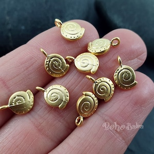 Könnte beinhalten: Nahaufnahme von zehn goldfarbenen Metall-Anhängern in Spiralform. Die Anhänger haben oben eine Öse zum Anbringen an Schmuck.