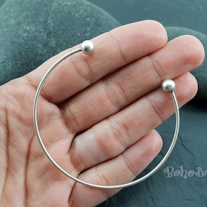 May include: A silver bangle bracelet with two round ball ends. The bracelet is open and has a simple design.