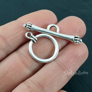 May include: Silver toggle clasp with a round ring and a bar with decorative ends. The clasp is designed for jewelry making.