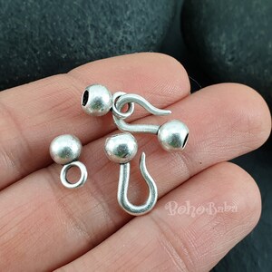 May include: Silver tone metal clasps with round balls. The clasps have a hook and loop design. The balls are about 1.2 cm in diameter.