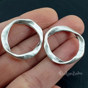 May include: Two silver-toned metal rings with a twisted, irregular shape. The rings are smooth and have a slightly textured surface.