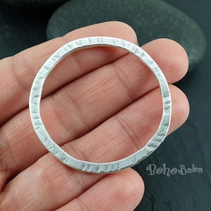 Può includere: Un ciondolo circolare in argento con una superficie testurizzata. Il ciondolo ha un diametro di circa 5 cm.