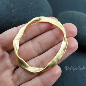 Puede incluir: Un colgante de anillo abierto de color dorado, retorcido. El anillo es liso y tiene una forma ligeramente irregular.