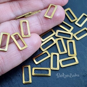 Op de afbeelding: Een grote hoeveelheid goudkleurige metalen rechthoekige springringen. De ringen zijn allemaal even groot en even gevormd en liggen in een stapel op een donker oppervlak.