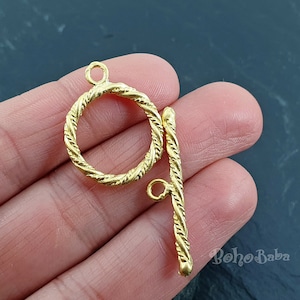 Puede incluir: Cierre de metal dorado con un anillo redondo y una barra recta. El cierre tiene un diseño de cuerda trenzada.