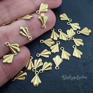 May include: A collection of gold-toned metal fan-shaped charms with a loop at the top. The charms are scattered on a dark surface.