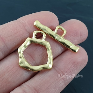 May include: Gold-toned metal clasp with a geometric shape and a rectangular bar. The clasp is designed for jewelry making or other craft projects.