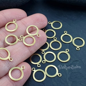 May include: A close-up of a hand holding a group of gold-colored metal jump rings. The jump rings are round with a small loop on one side. The rings are arranged in a random pattern on the hand.
