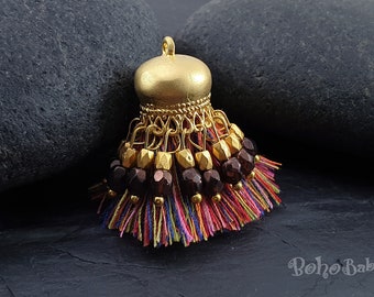 May include: A gold tassel with brown and gold beads and multi-colored threads. The tassel is on a black background.