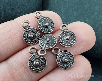 May include: Six antique copper-toned metal charms with a circular design and a small loop at the top. Each charm has a raised, concentric circle pattern with a smaller circle in the center.