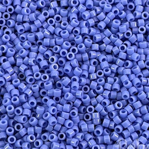 May include: A close-up shot of a pile of small, cylindrical beads in a soft periwinkle blue color. The beads are uniform in size and shape, with a hole running through the center of each one. These beads are ideal for jewelry making and crafts.