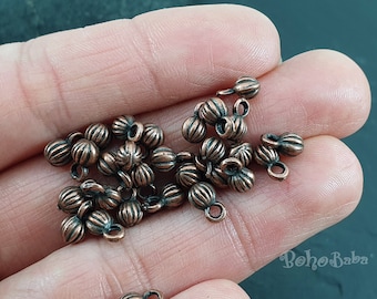 May include: A pile of small, copper-colored metal beads with a decorative, ribbed design. Each bead has a small loop at the top for attaching to jewelry or other crafts.