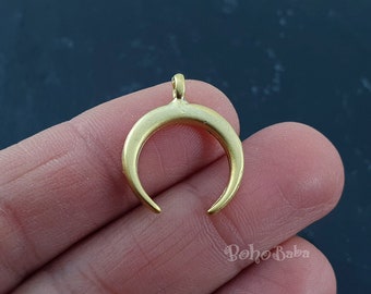 May include: A gold-colored crescent moon pendant with a loop at the top for hanging. The pendant has a matte finish and a curved shape. The background is a dark, mottled surface.