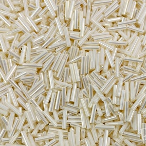 May include: A large quantity of small, white, iridescent glass beads in the shape of long cylinders. The beads are scattered randomly and appear to be made of glass.