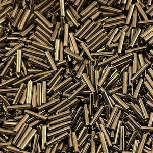 Op de afbeelding: Een close-up van een grote hoeveelheid goudkleurige glazen kralen. De kralen zijn lang en cilindrisch, en lijken op kleine buisjes.