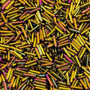 May include: A large pile of iridescent gold and purple glass beads. The beads are long and cylindrical, resembling small tubes.