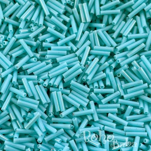 Może przedstawiać: Duża ilość turkusowych szklanych koralików w kształcie rurki. Koraliki są rozrzucone losowo.