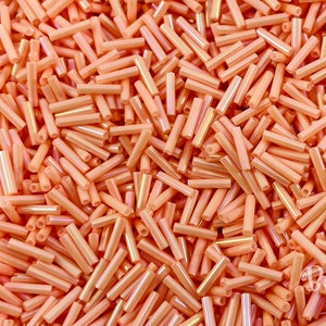 Puede incluir: Un montón grande de pequeñas cuentas de vidrio naranja. Las cuentas son iridiscentes y tienen un brillo ligeramente metálico.