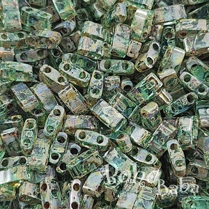 May include: A close-up image of a large quantity of small, green, iridescent glass beads. The beads are rectangular in shape with two holes on each side.