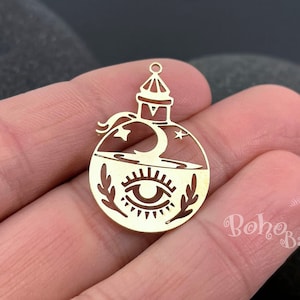 May include: Gold metal charm shaped like a bottle with a crescent moon, stars, and an eye inside. The charm has a loop at the top for attaching to jewellery.