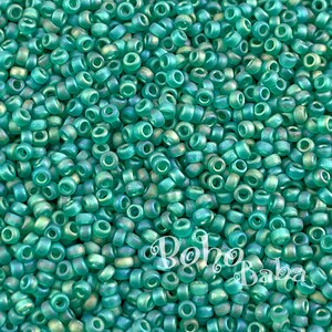 May include: A close-up image of a large quantity of small, round, teal-colored glass beads. The beads have a slightly iridescent finish.