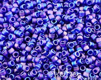 May include: A close-up view of a large quantity of small, round, blue and purple glass beads. The beads have a metallic sheen and are arranged in a random pattern.