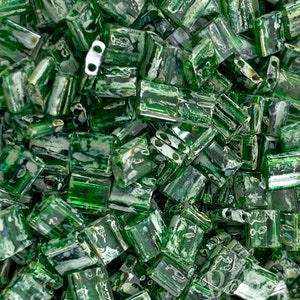 Puede incluir: Una imagen de primer plano de un montón de cuentas de vidrio verde con un efecto de mármol blanco. Las cuentas son de forma rectangular y tienen un agujero en el centro para enhebrar.