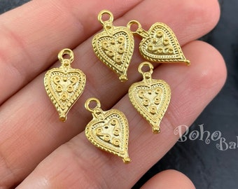 May include: Five gold-toned heart-shaped charms with intricate embossed details. The charms have a loop at the top for attaching to jewelry or other crafts.