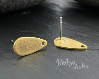 May include: Two gold-toned teardrop-shaped earring blanks with a small hole at the top. The earring blanks are on a dark gray surface.