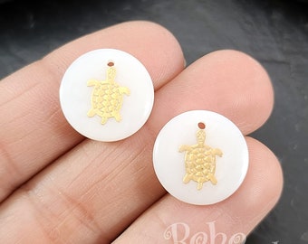 May include: Two white round ceramic charms with a gold turtle design. The charms have a hole at the top for hanging.