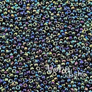 Op de afbeelding: Een close-up van een grote hoeveelheid iriserende zwarte zaadkraaltjes. De kralen hebben een metallic glans en reflecteren een verscheidenheid aan kleuren, waaronder blauw, groen en paars.