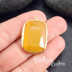May include: A gold-toned pendant with a rectangular, yellow-amber gemstone. The pendant has a textured gold border.