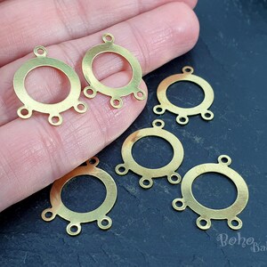 Può includere: Sei componenti per orecchini in metallo dorato con un design circolare e cinque anelli ciascuno. I componenti sono su una superficie scura.