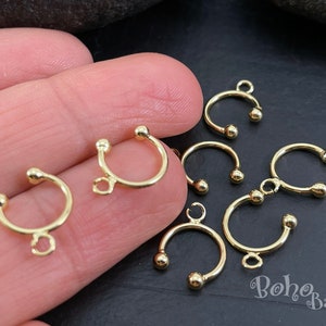 May include: Gold-toned metal hoops with a small loop on one side. The hoops have a rounded shape and are approximately 2.5 cm in diameter.
