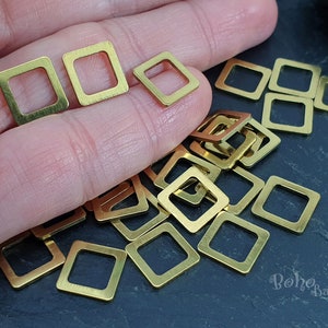 May include: A large pile of gold-coloured metal square jump rings. The jump rings are about 1.25 cm in diameter.