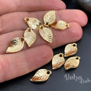 Könnte beinhalten: Goldene Blatt-Anhänger mit strukturierter Oberfläche und einem Loch zum Aufziehen. Die Anhänger sind blattförmig und etwa 2,5 cm lang.