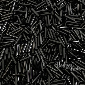 Op de afbeelding: Een grote stapel zwarte glazen kralen, elke kraal heeft een langwerpige cilinder vorm.