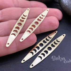 Può includere: Quattro ciondoli in metallo color oro a forma di mezzaluna con un designo a taglio. I ciondoli sono su una mano e una superficie scura. Il testo "boho baba" è visibile nell'angolo in basso a destra dell'immagine.