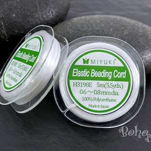 May include: Two spools of white elastic beading cord, each in a clear plastic container with a green and white label. The label reads "MIYUKI Elastic Beading Cord H3198E 5m(5.5yds) 0.6~0.8mm dia 100% Polyurethane Made in Japan."