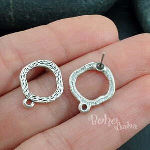 May include: Two silver earring blanks with a textured, square-shaped design. Each blank has a small loop at the bottom and a post at the top.