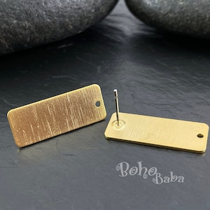 Peut inclure: Une paire de supports de boucles d'oreilles rectangulaires dorés avec une finition brossée. Chaque support a un trou en haut et un poteau à l'arrière.