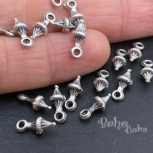 Puede incluir: Encantos de metal plateado con un diseño decorativo. Los encantos tienen un pequeño bucle en la parte superior y un bucle más grande en la parte inferior. Los encantos están dispersos sobre una superficie oscura.