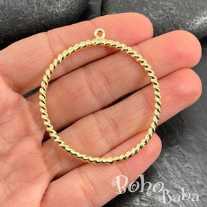 May include: A gold-colored, twisted-rope design hoop earring. The earring has a small loop at the top for attachment. The Boho Baba logo is visible in the lower right corner. The earring is held in a hand.