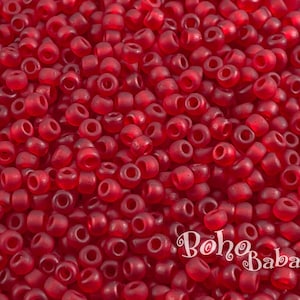 May include: A close-up image of a large quantity of small, round, red glass beads. The beads are opaque and have a slightly frosted finish.