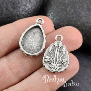 Peut inclure: Deux breloques pendantes en forme de goutte d'eau argentées. Un charme a une surface lisse et arrondie, tandis que l'autre a un motif gravé d'une fleur avec une tige et des feuilles.