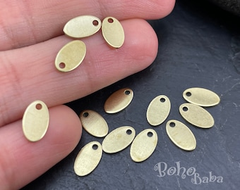 May include: A collection of 10 oval-shaped brass charms with a hole at the top. The charms are a light gold color and have a brushed finish.