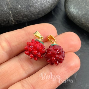 Puede incluir: Dos abalorios de fruta de esmalte rojo y verde con un cierre de oro. Los abalorios tienen forma de frambuesa y una superficie texturizada.